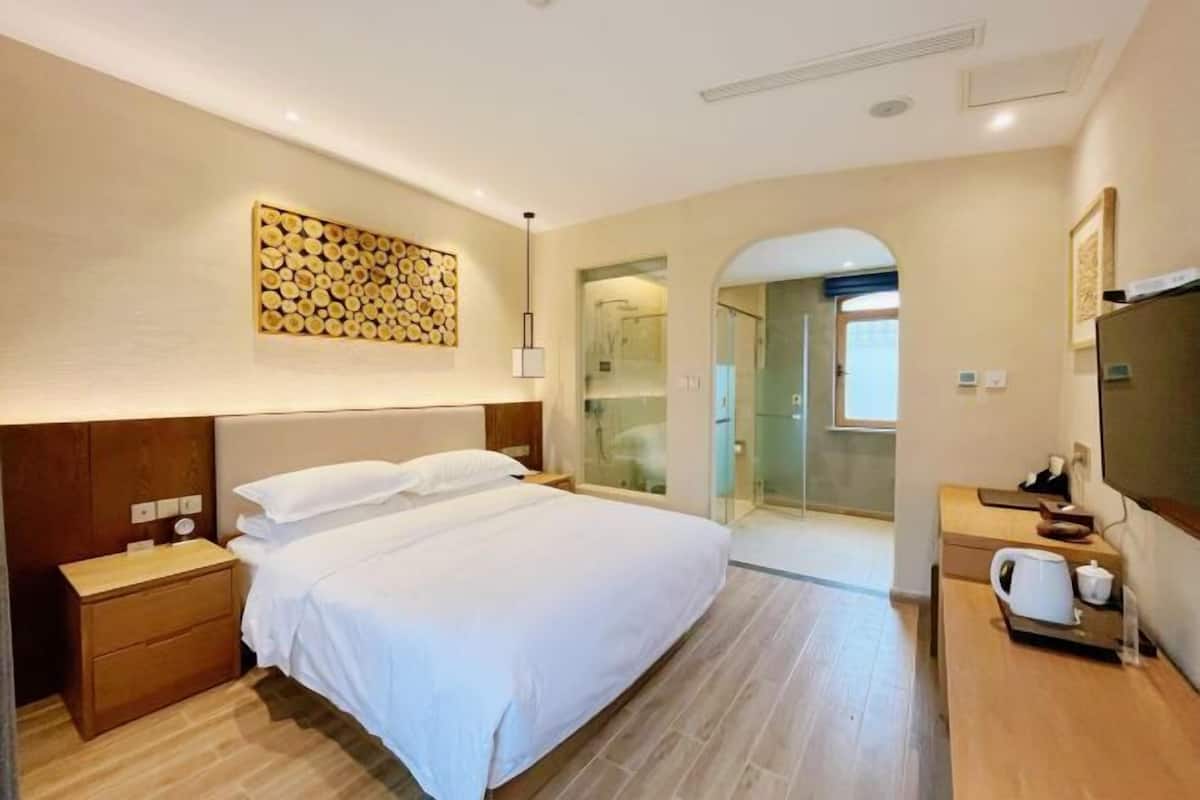 A hotel room with a bed, bedside table, a mirror, a towel rack, and a shower area.