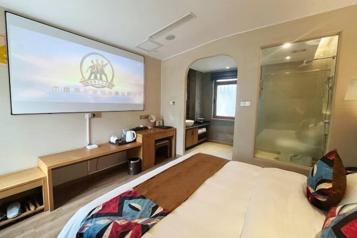 A modern hotel room with a TV, a bed, a shower, and a desk.