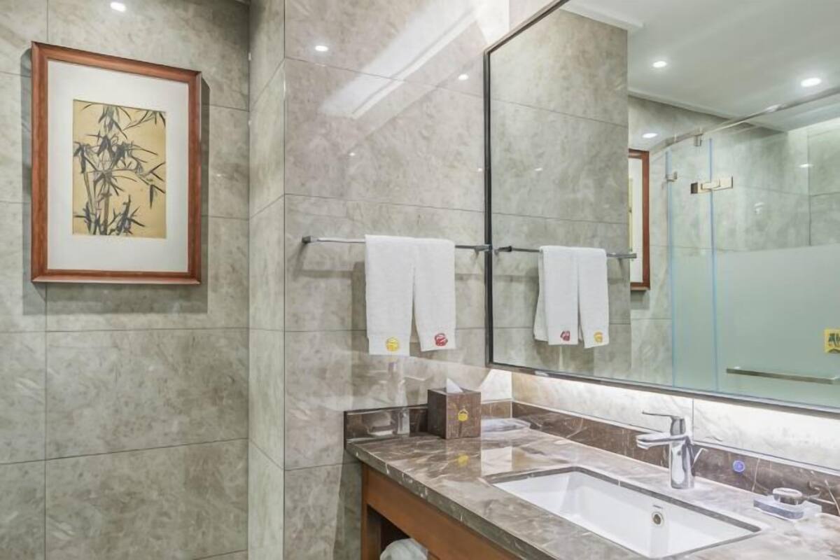 A bathroom with a marble sink, a large mirror, and a framed artwork on the wall.