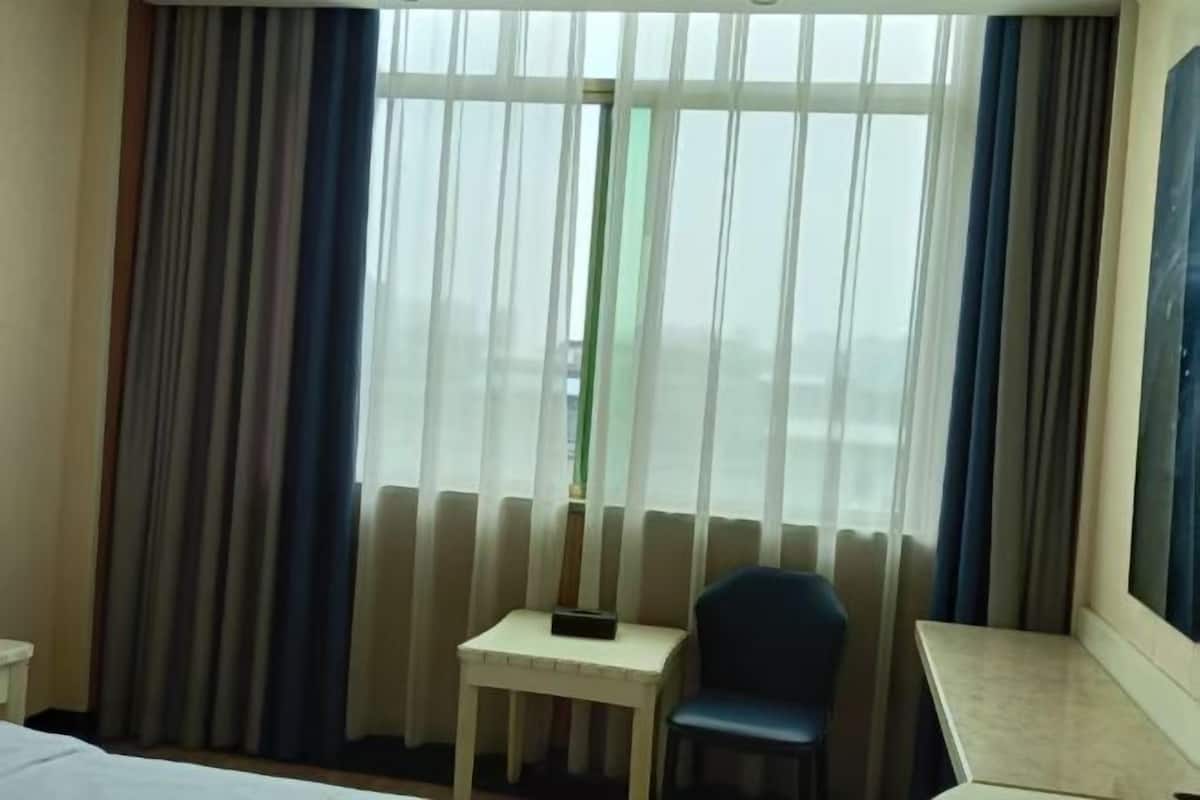 A hotel room with a bed, a small table, a chair, and a window with curtains.