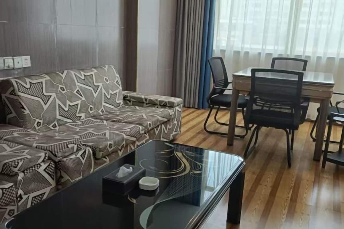 A living room with a patterned sofa, a glass coffee table, and a dining area with a table and chairs.