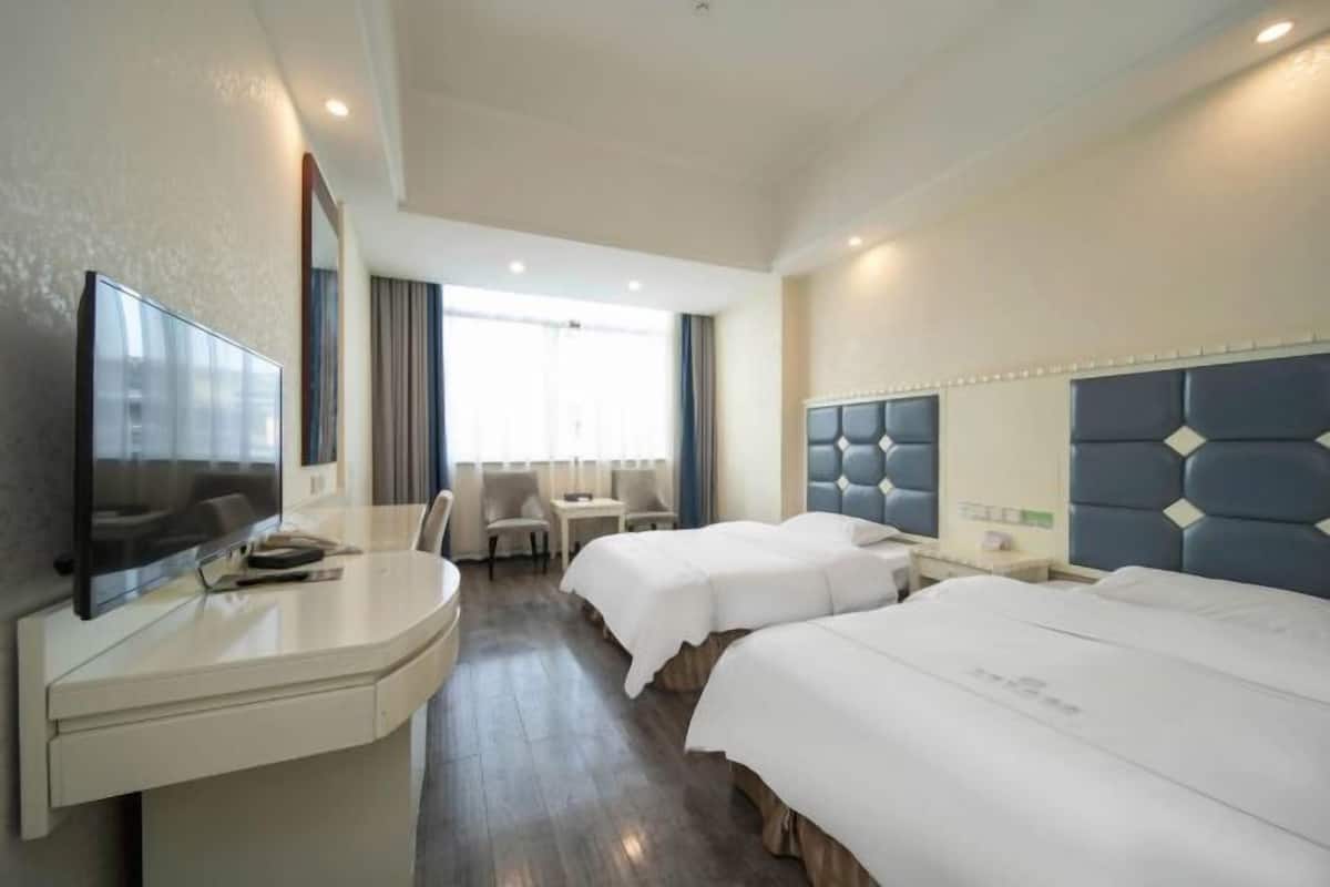 A hotel room with a desk, two beds, a TV, and a window with curtains.