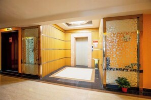 Een hotellobby met een receptiebalie, een glazen lift en een deur met een decoratief patroon.