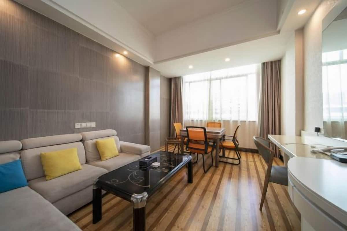 A modern living room with a sofa, a coffee table, a dining area with chairs, and a kitchen counter.