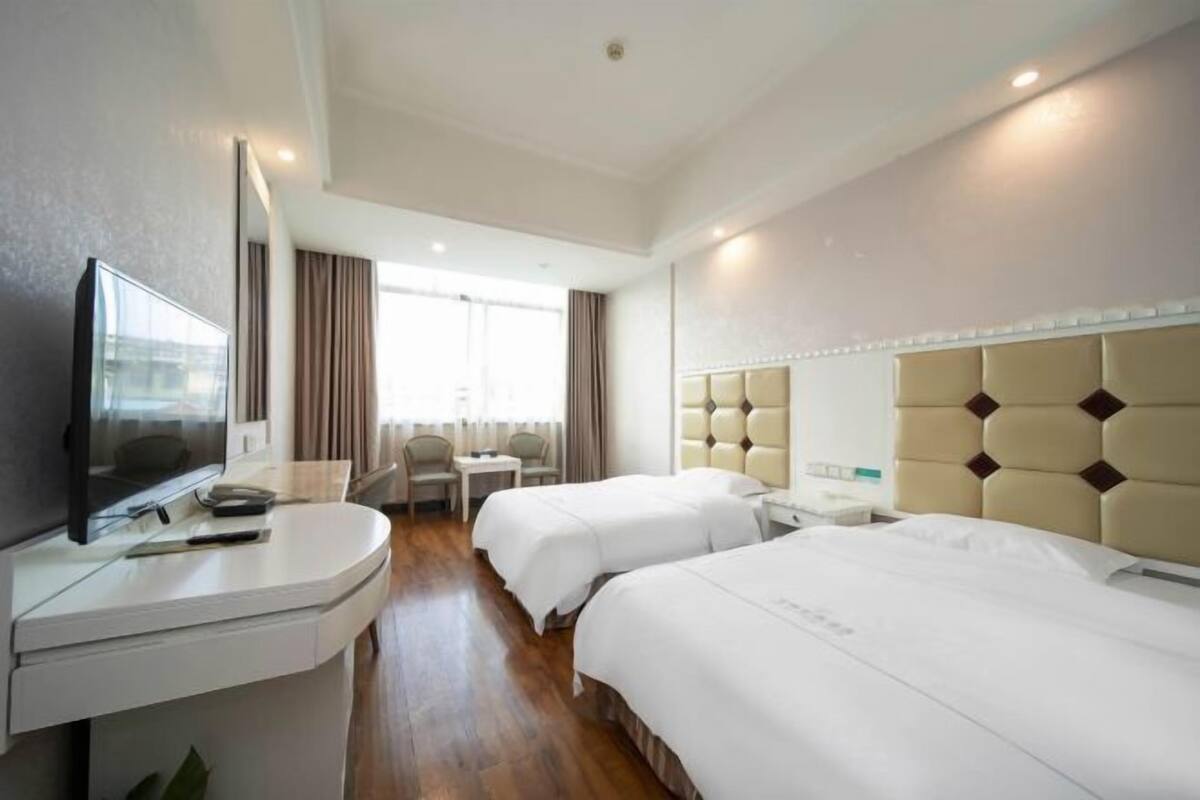 A hotel room with two beds, a desk with a flat-screen TV, a chair, and a small table.