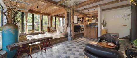 Un amplio salón con techo de madera, suelo de baldosas hexagonales y una zona de estar con sofá y mesa de comedor.