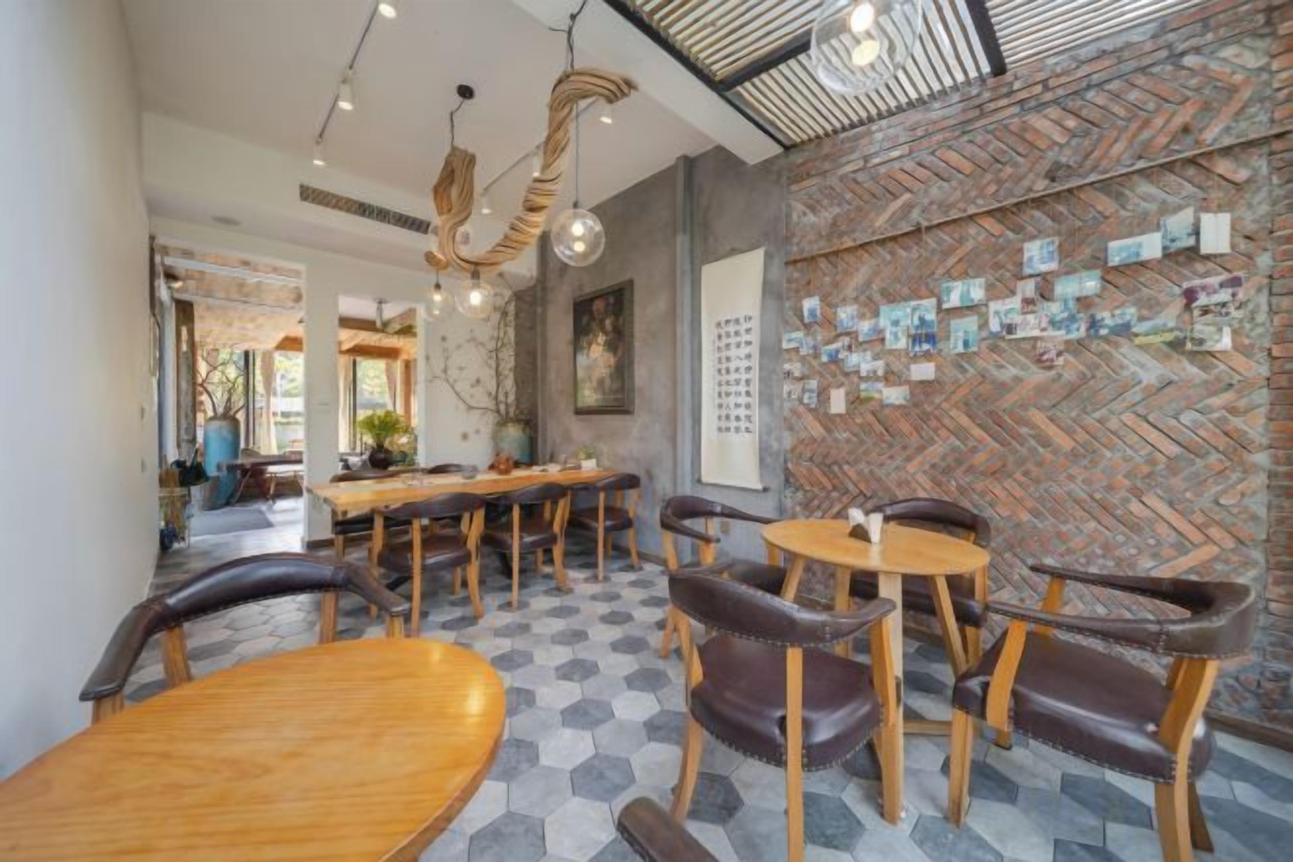 A restaurant interior with hexagonal patterned flooring, wooden tables and chairs, and a brick wall with pinned notes.
