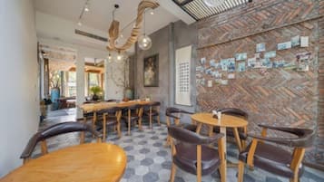 A restaurant interior with hexagonal patterned flooring, wooden tables and chairs, and a brick wall with pinned notes.