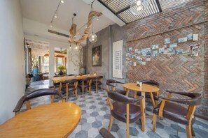 Een restaurantinterieur met hexagonaal patroon op de vloer, houten tafels en stoelen, en een bakstenen muur met spelden en briefjes.