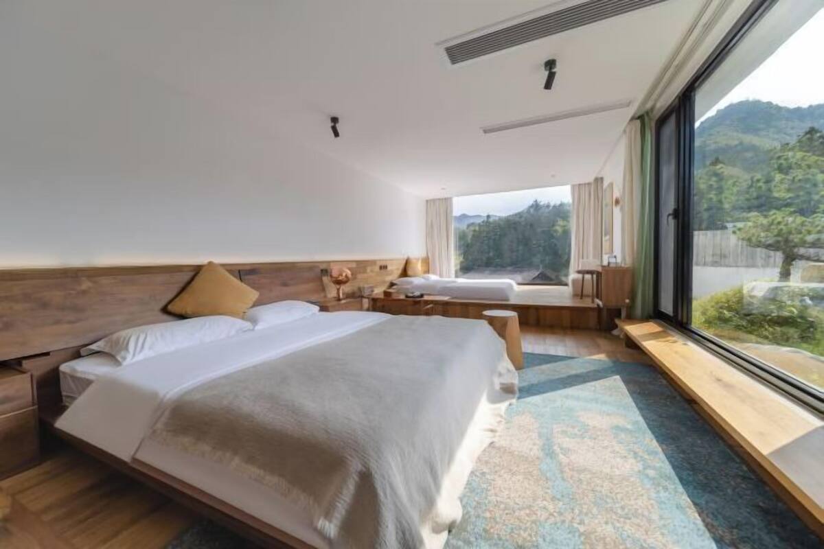 Een moderne slaapkamer met een groot bed, een houten hoofdbord en een uitzicht op een bergachtig landschap door een groot raam.