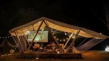 A tent-like structure with a flat roof, a projection screen, and string lights.