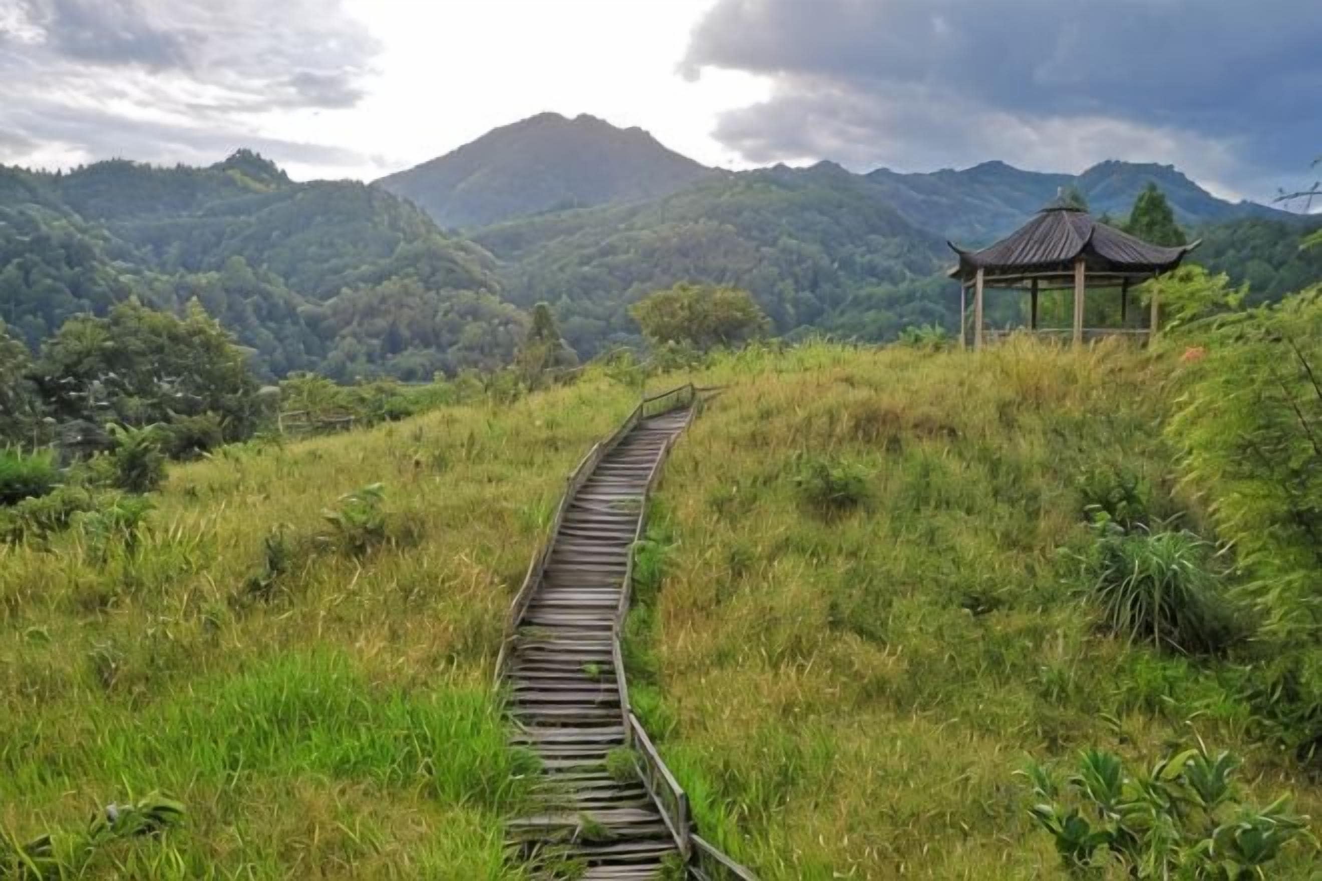A wooden pathway leading to a traditional gazebo in a mountainous area.