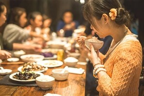 Una persona sentada en una mesa de madera con varios platos, evocando un ambiente de comedor compartido.