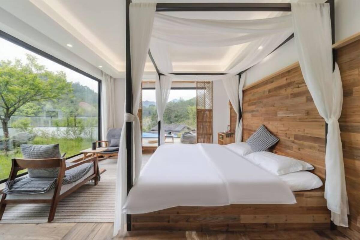 Een slaapkamer met een groot bed, een houten hoofdbord en uitzicht op groen.