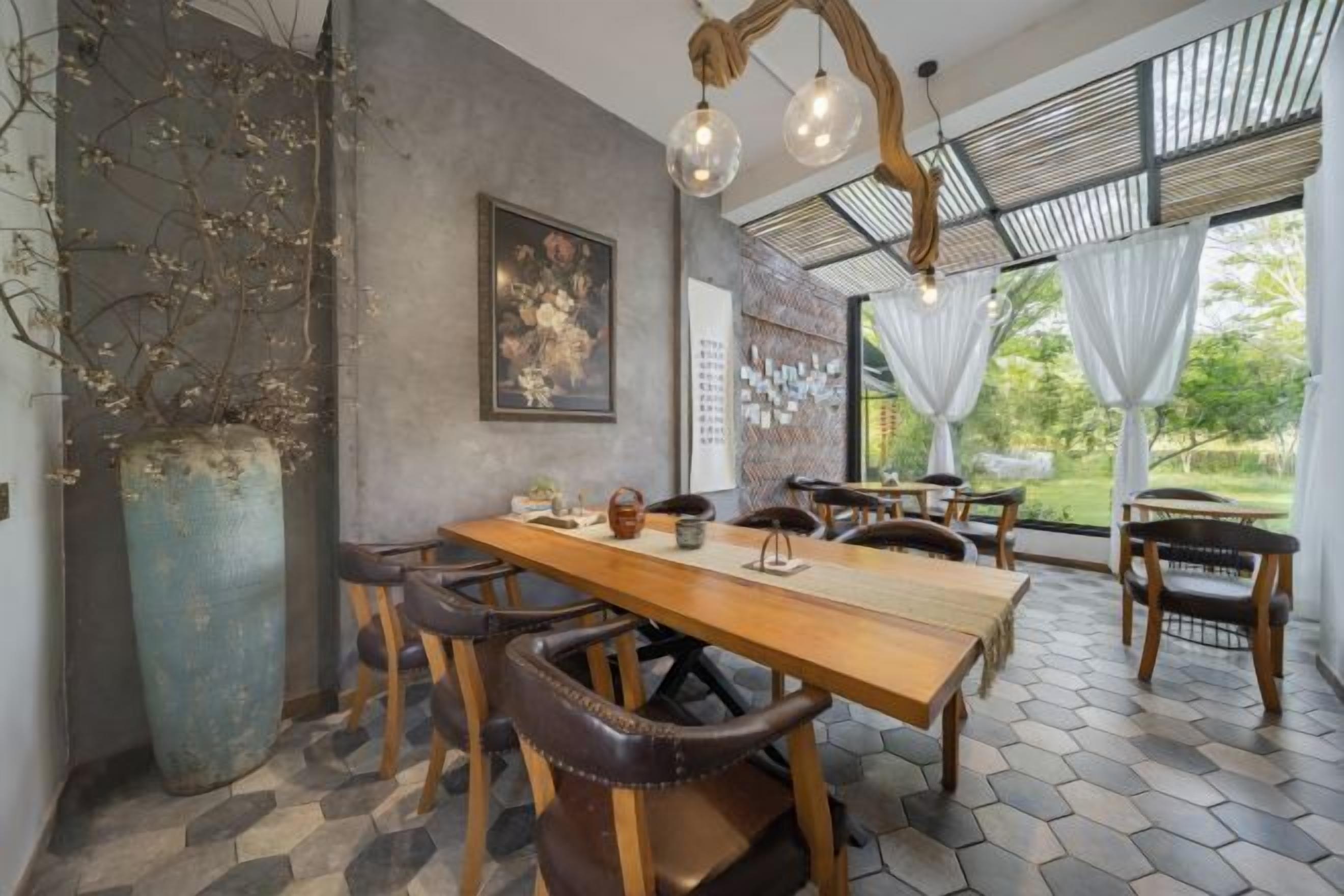 Un espace repas comprenant une longue table en bois, plusieurs chaises, un grand vase et un luminaire suspendu.