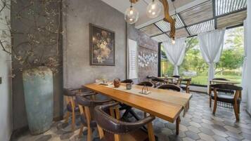 Un espace repas comprenant une longue table en bois, plusieurs chaises, un grand vase et un luminaire suspendu.