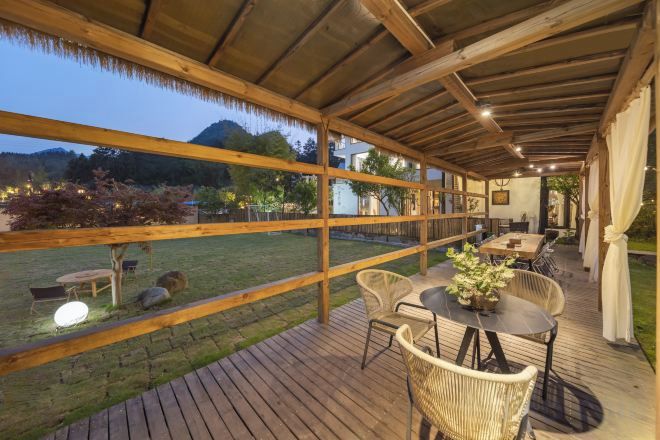 An outdoor patio with a wooden deck, wicker furniture, and a table with a vase of flowers.