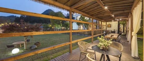 Un patio exterior con cubierta de madera, mobiliario de mimbre y una mesa con un florero.