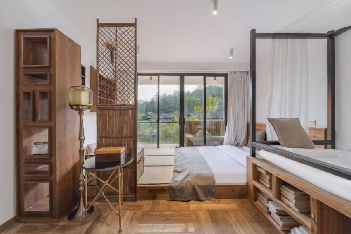 Een slaapkamer met een bed, een bureau, een stoel, een boekenkast en uitzicht op de omgeving.