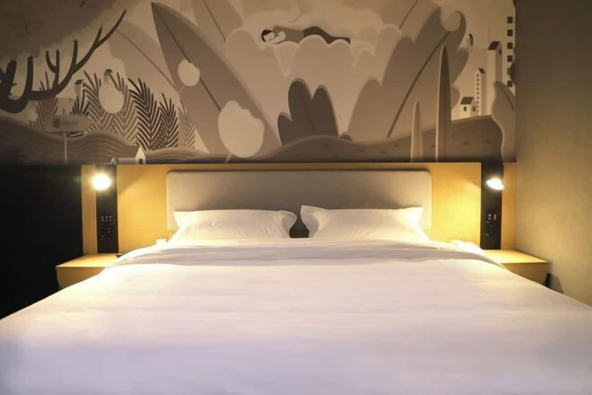 A hotel room with a large bed, two bedside tables, and a wall mural.