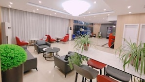 A modern hotel lobby with a seating area, a reception desk, and a large chandelier.