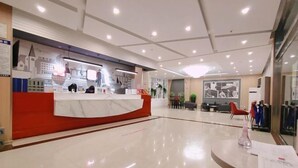 A hotel reception area with a red counter, a polished floor, and a seating area with chairs and tables.