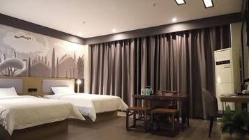 Quarto de hotel com duas camas, uma escrivaninha, uma cadeira e uma janela grande com cortinas.