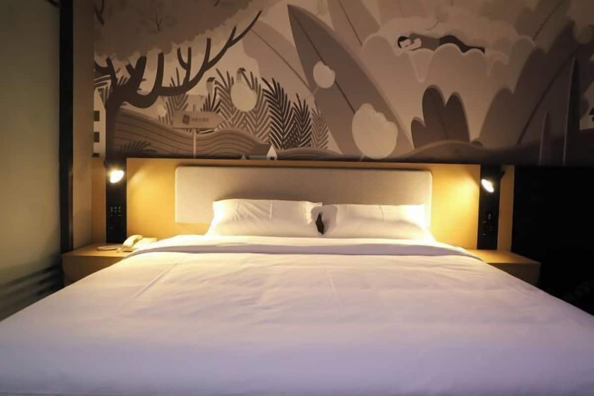 A hotel room with a large bed, a headboard with integrated lighting, a nightstand with a phone, and a wall mural.