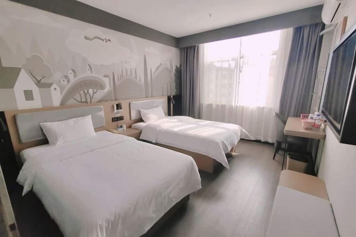 A hotel room with two beds, a desk, a chair, and a large window with curtains.