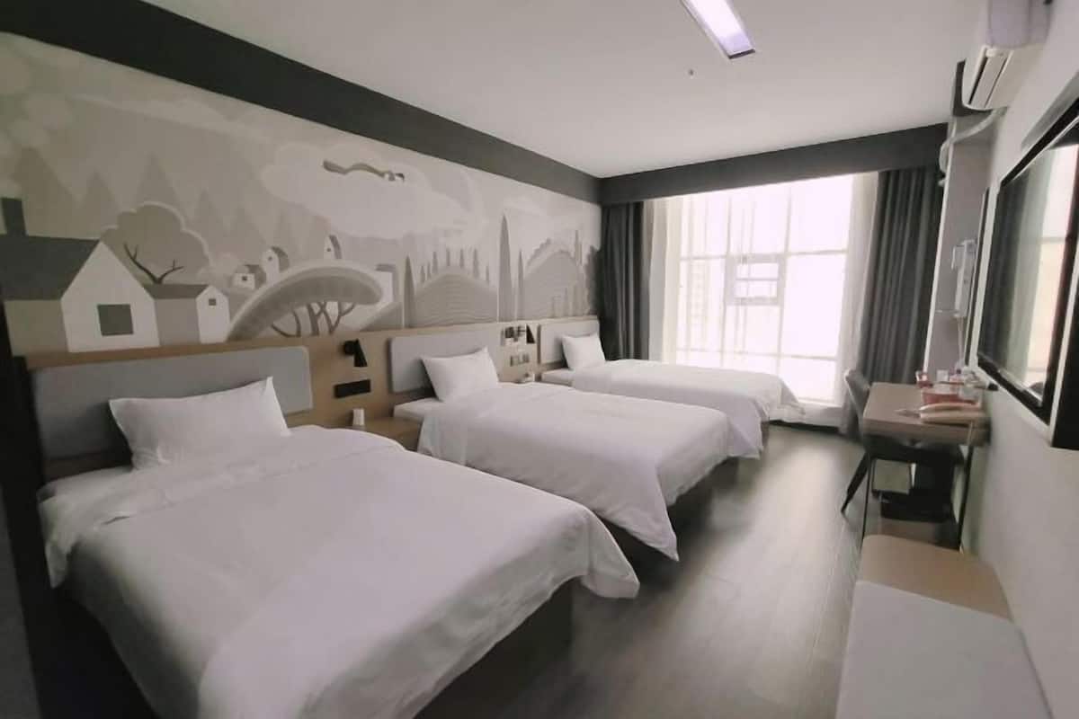 A hotel room with three beds, a desk, and a large window.