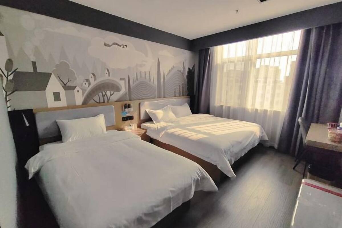 A hotel room with two beds, a desk, and a large window with curtains.