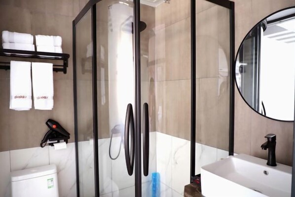 Une salle de bain moderne avec une douche à parois de verre, un lavabo blanc doté d’un robinet noir et un miroir au-dessus du lavabo.
