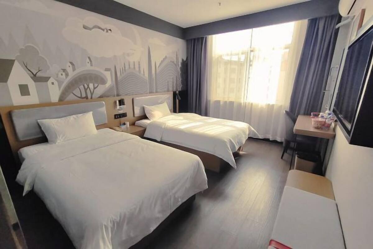 A hotel room with two beds, a desk, and a large window with curtains.
