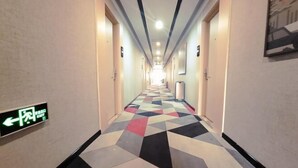 A hotel hallway with a geometric patterned floor, directional signs, and a bright ceiling light.