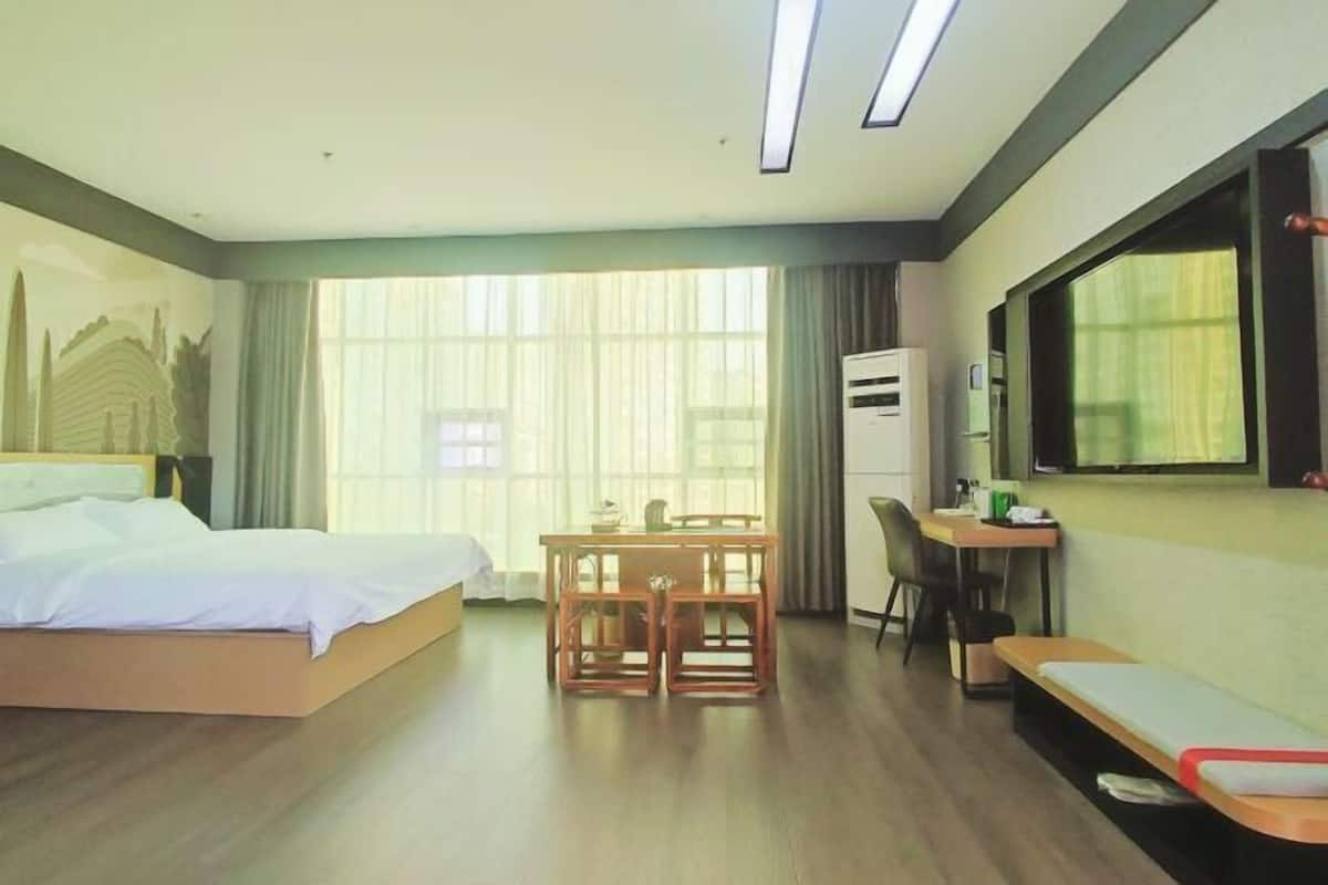 A hotel room with a bed, a desk, a chair, a small table, and a TV.