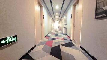 Un pasillo de hotel con piso de diseño geométrico, indicaciones y puertas a ambos lados.