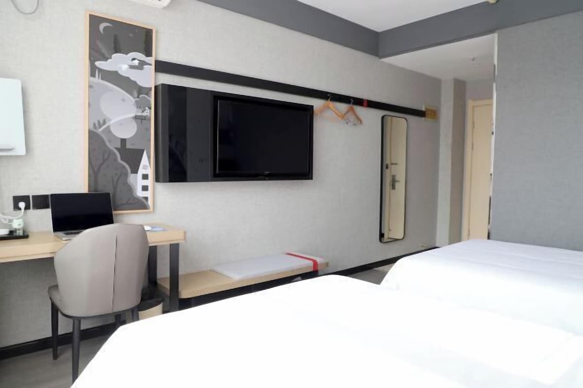 Une chambre d’hôtel avec un lit, un bureau équipé d’un ordinateur, un téléviseur fixé au mur et un miroir.
