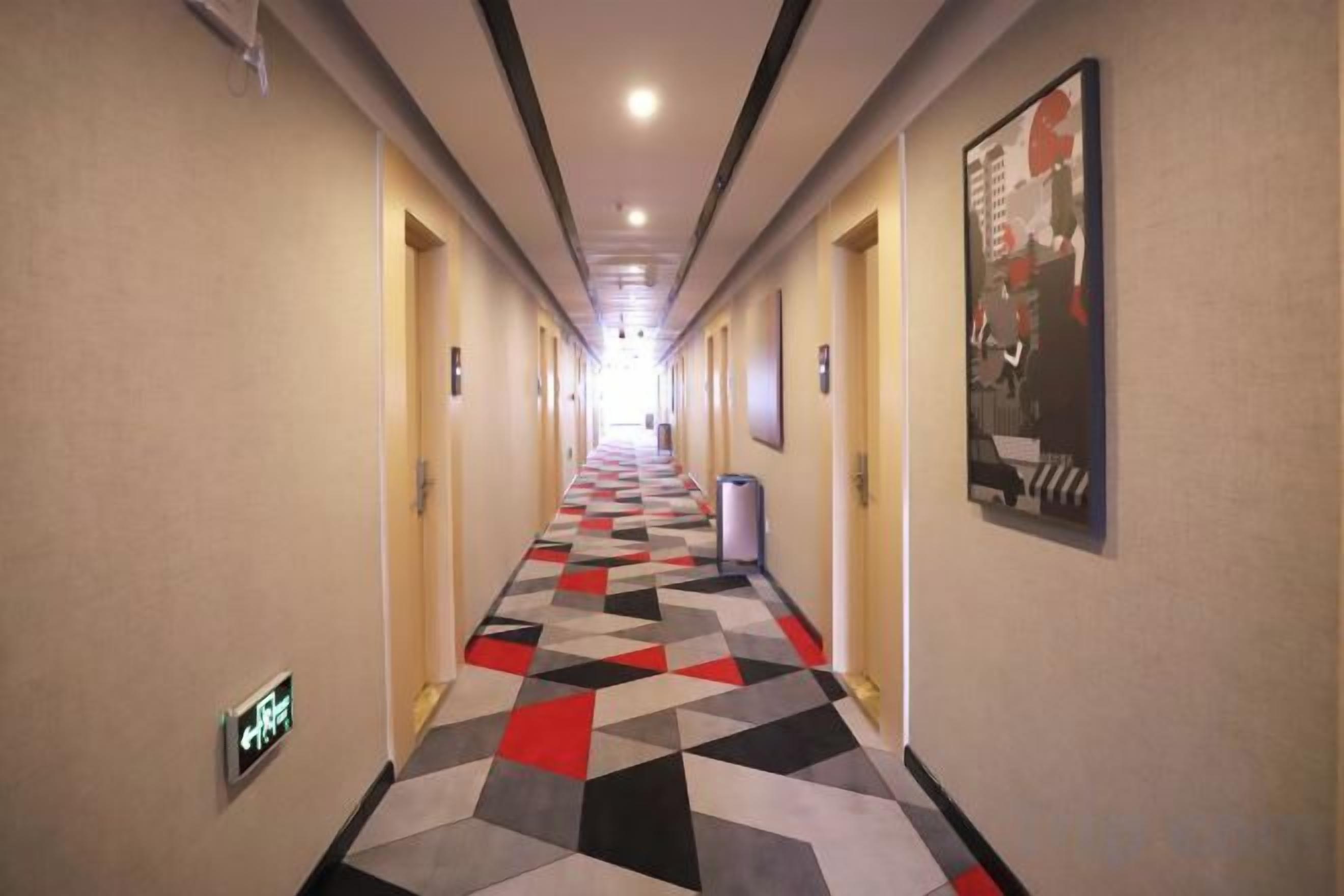 Un pasillo de hotel con piso de diseño geométrico, puertas a ambos lados y un cartel en la pared derecha.