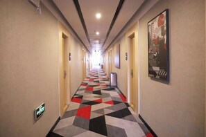 A hotel hallway with a geometric patterned floor, doors on both sides, and a poster on the right wall. - Shankee Hotel (Tancheng Sifang Furniture Plaza) (Tancheng)