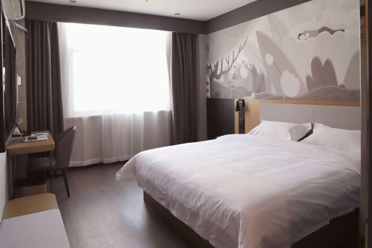 Une chambre d’hôtel avec un grand lit, un bureau et une fenêtre avec des rideaux.