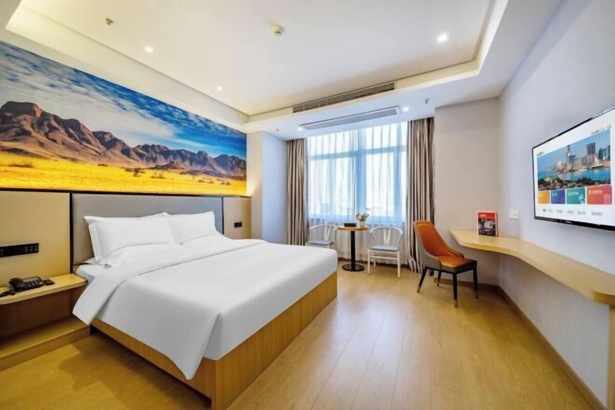 A hotel room with a large bed, a desk, a chair, a TV, and a painting on the wall.
