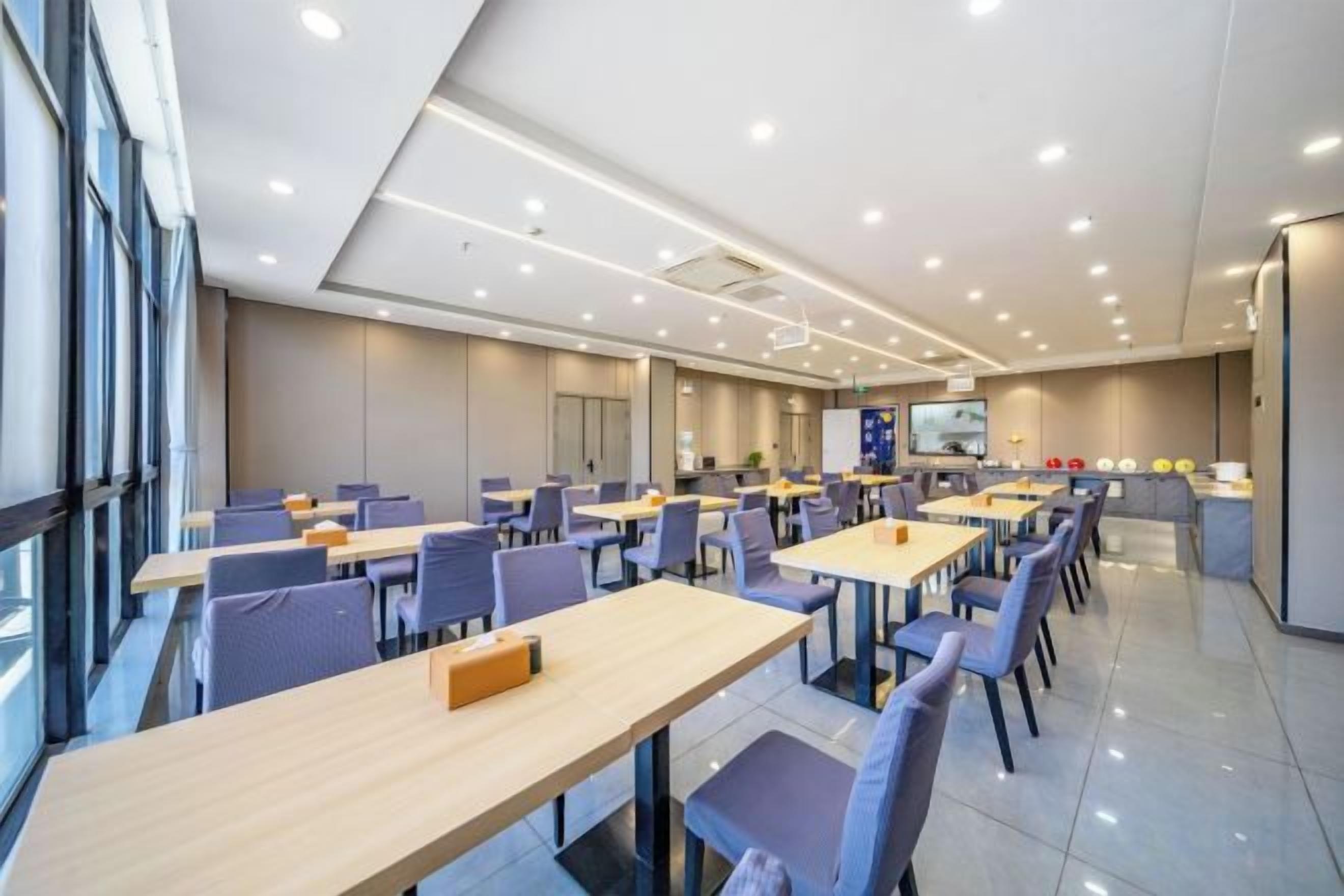 A modern dining area with multiple tables and chairs, a kitchen area, and a large window providing natural light.