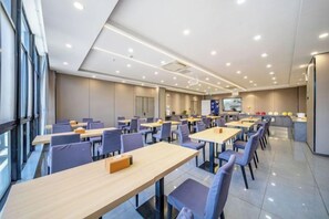 A modern dining area with multiple tables and chairs, a kitchen area, and a large window providing natural light. - Home Inn Subayun (Rugao)