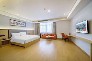 Una habitación de hotel con cama, sofá, una mesita, una silla y televisión en la pared.