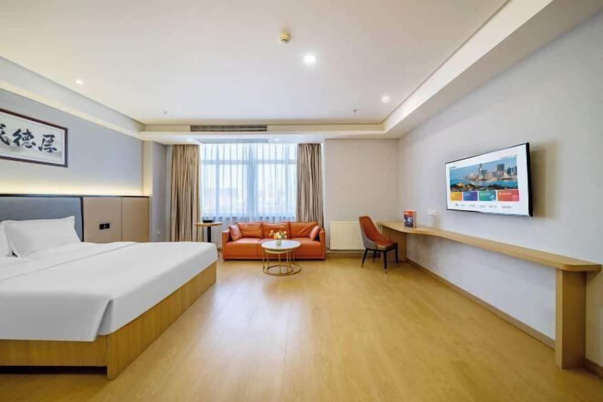 A hotel room with a bed, a sofa, a small table, a chair, a TV, and a window with curtains.