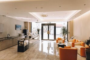 A modern hotel lobby with a marble floor, a reception desk, and orange seating. - Home Inn Subayun (Rugao)