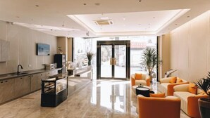 A modern hotel lobby with a marble floor, a reception desk, a seating area with orange sofas, and a large glass door leading outside. - Home Inn Subayun (Rugao)