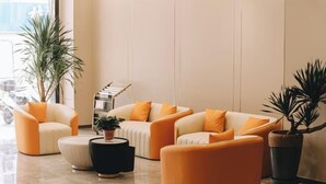 A modern lobby with a seating area featuring orange and white sofas, a black coffee table, and potted plants. - Home Inn Subayun (Rugao)