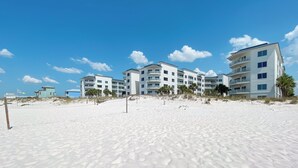 A beachfront hotel with multiple floors, a sandy beach in the foreground, and a clear blue sky. - BEACHFRONT RESORT, FAMILY FRIENDLY, TOP AMENITIES (Orange Beach)