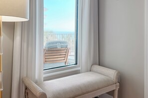 Un rincón con un banco, una ventana con cortinas y vistas a una terraza de madera.